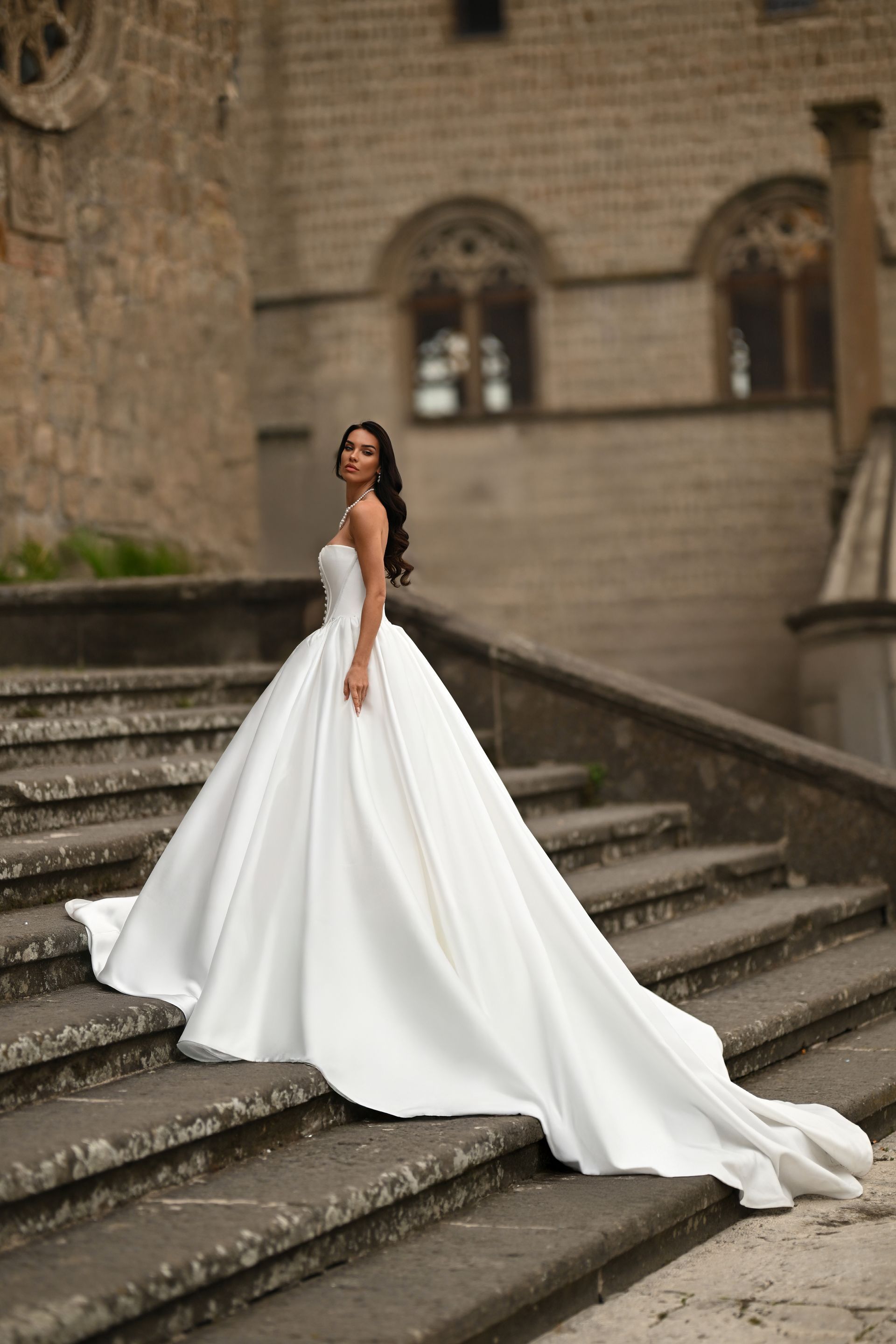 Bride in a flowing white gown standing on stone steps beside an old stone building