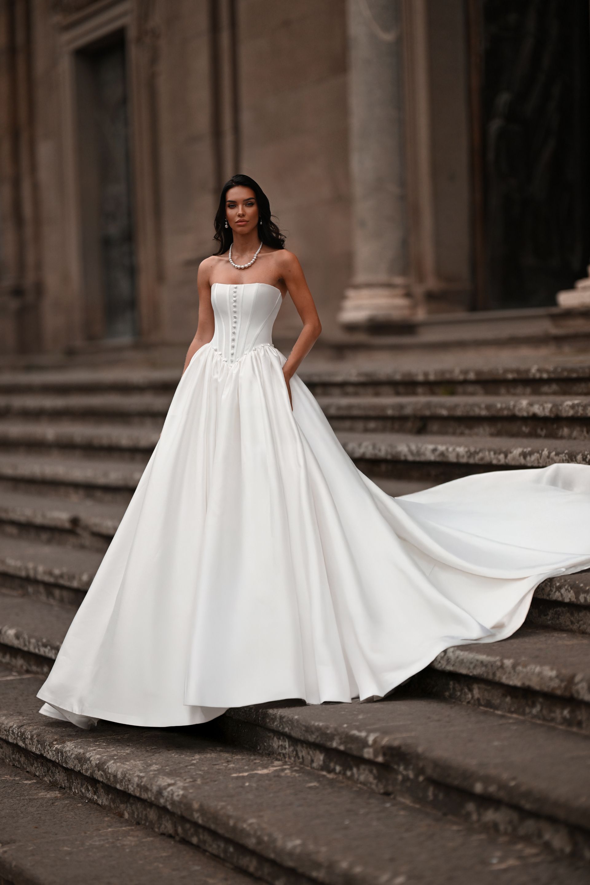 Woman in a white strapless gown standing on stone steps with a long flowing train.