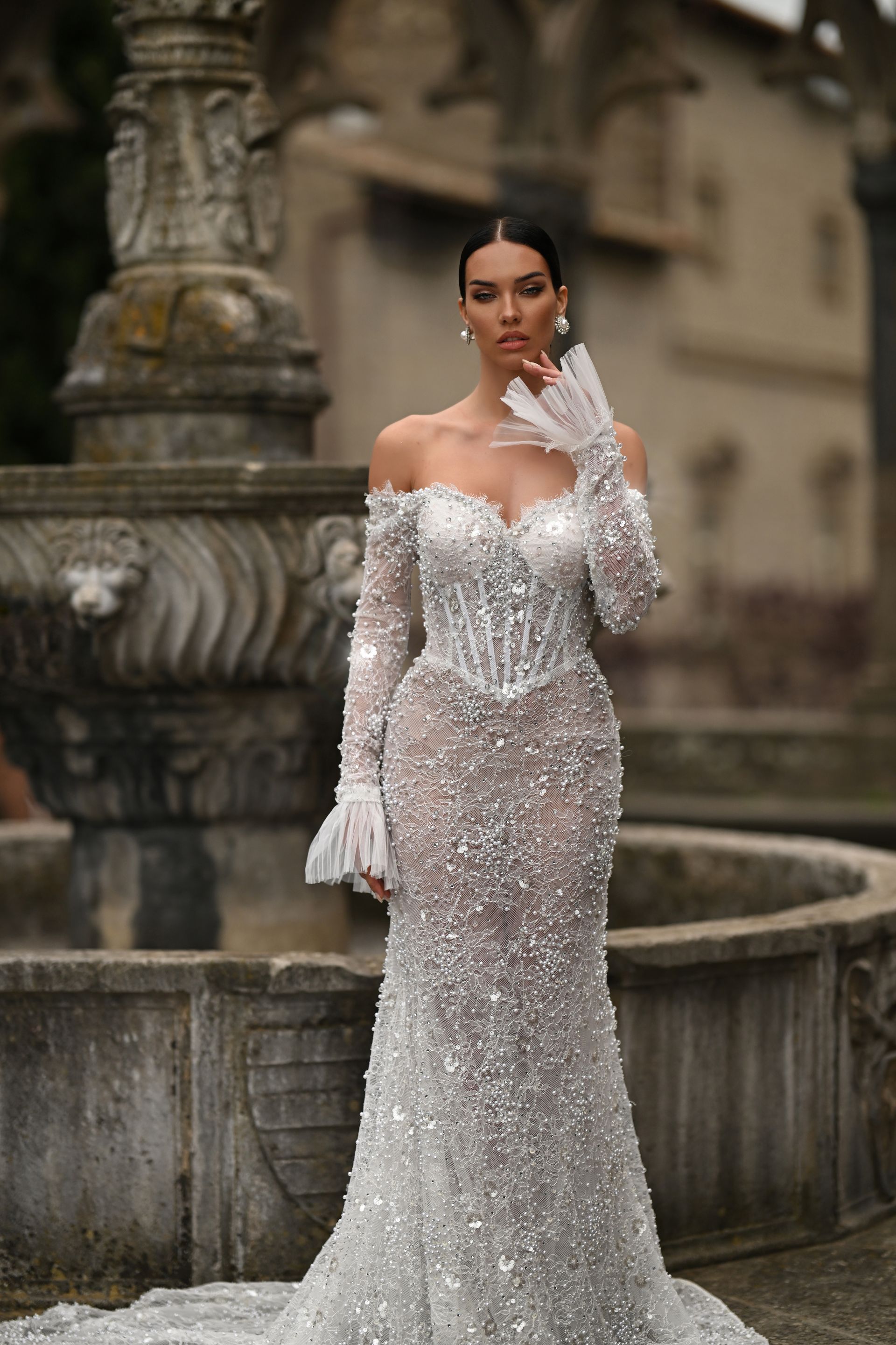 Woman in a sparkling silver gown posing by a fountain in a historic courtyard