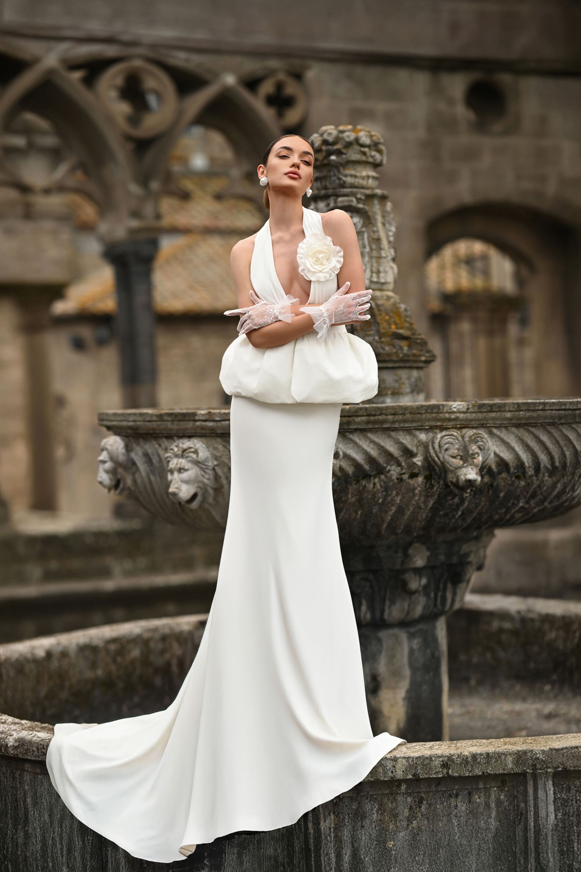Woman in a white gown posing by a stone fountain in a historic courtyard