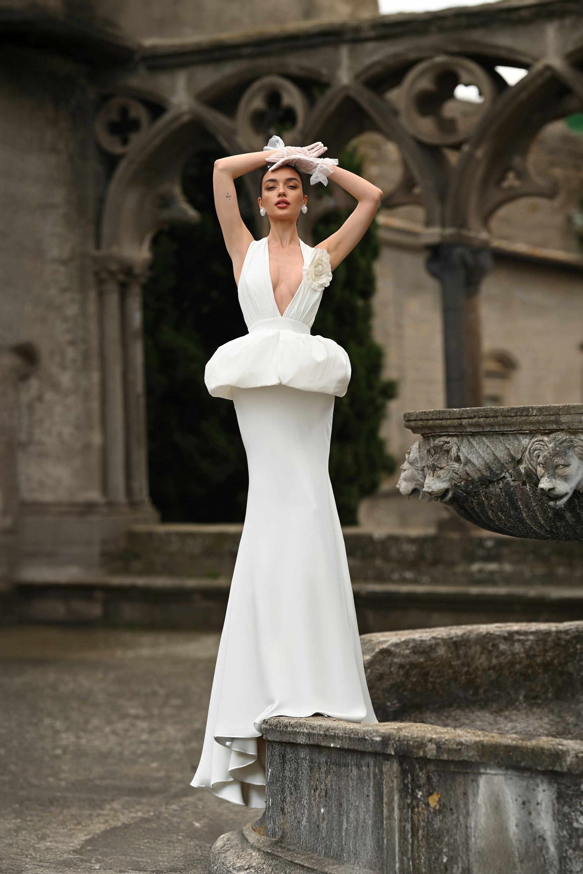 Woman in a white gown and floral headpiece posing in a stone courtyard garden