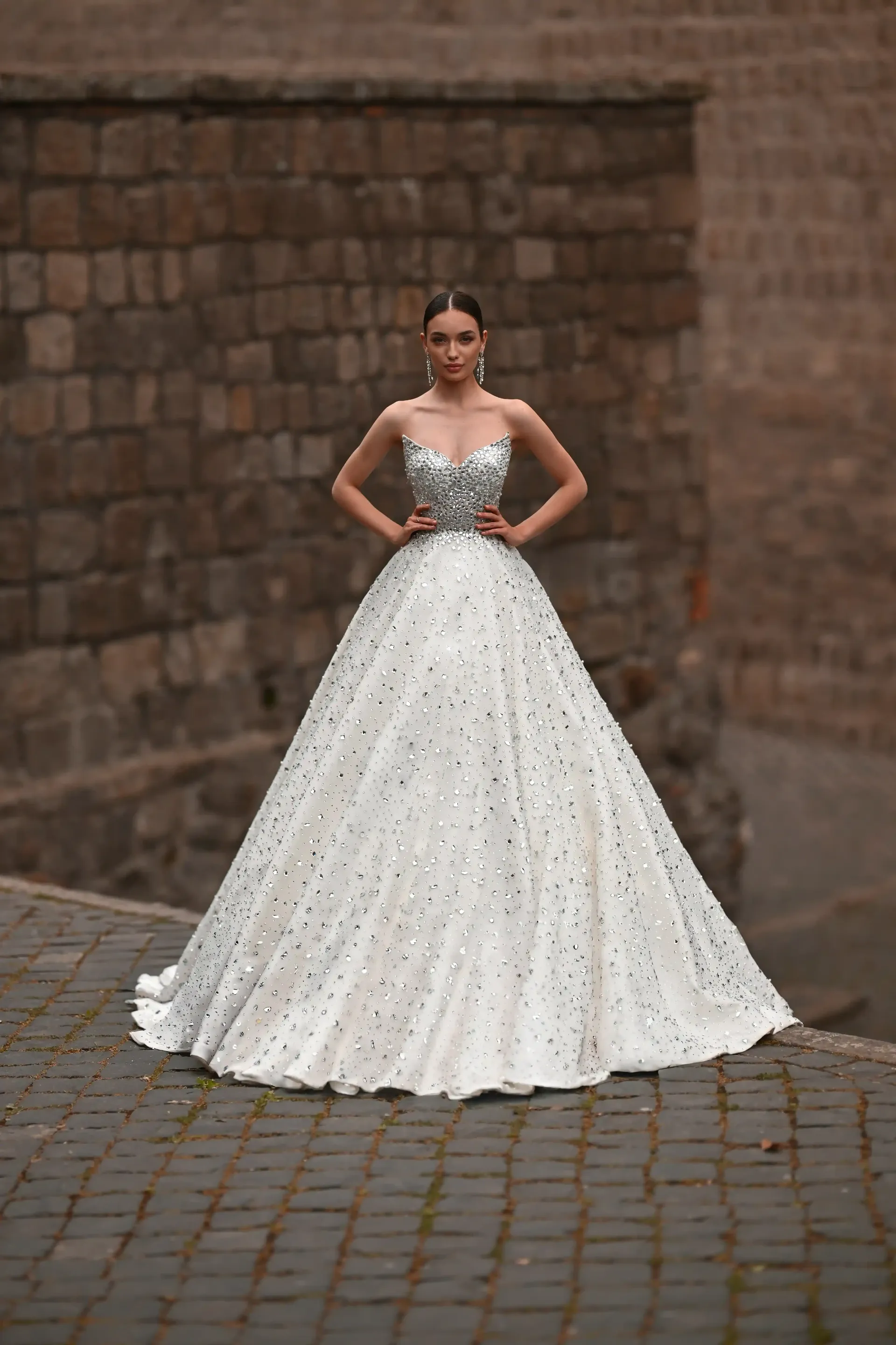 Woman in a white sequined gown standing on cobblestones before a brick wall