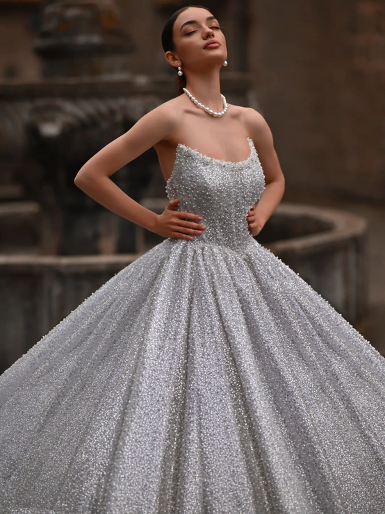 Woman in a sparkling silver ball gown posing outdoors with hands on hips.