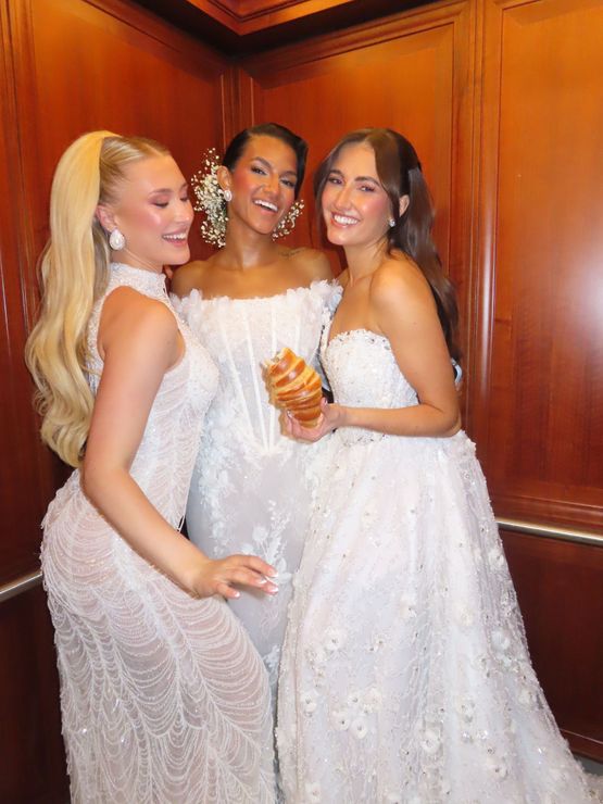 Three women in white dresses smiling and posing together at a formal event