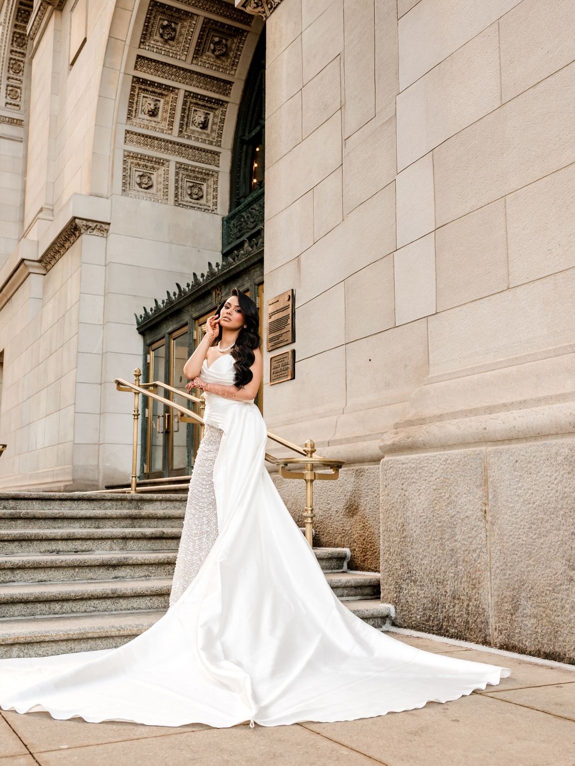Woman in a white gown posing on stone steps beside an ornate building entrance