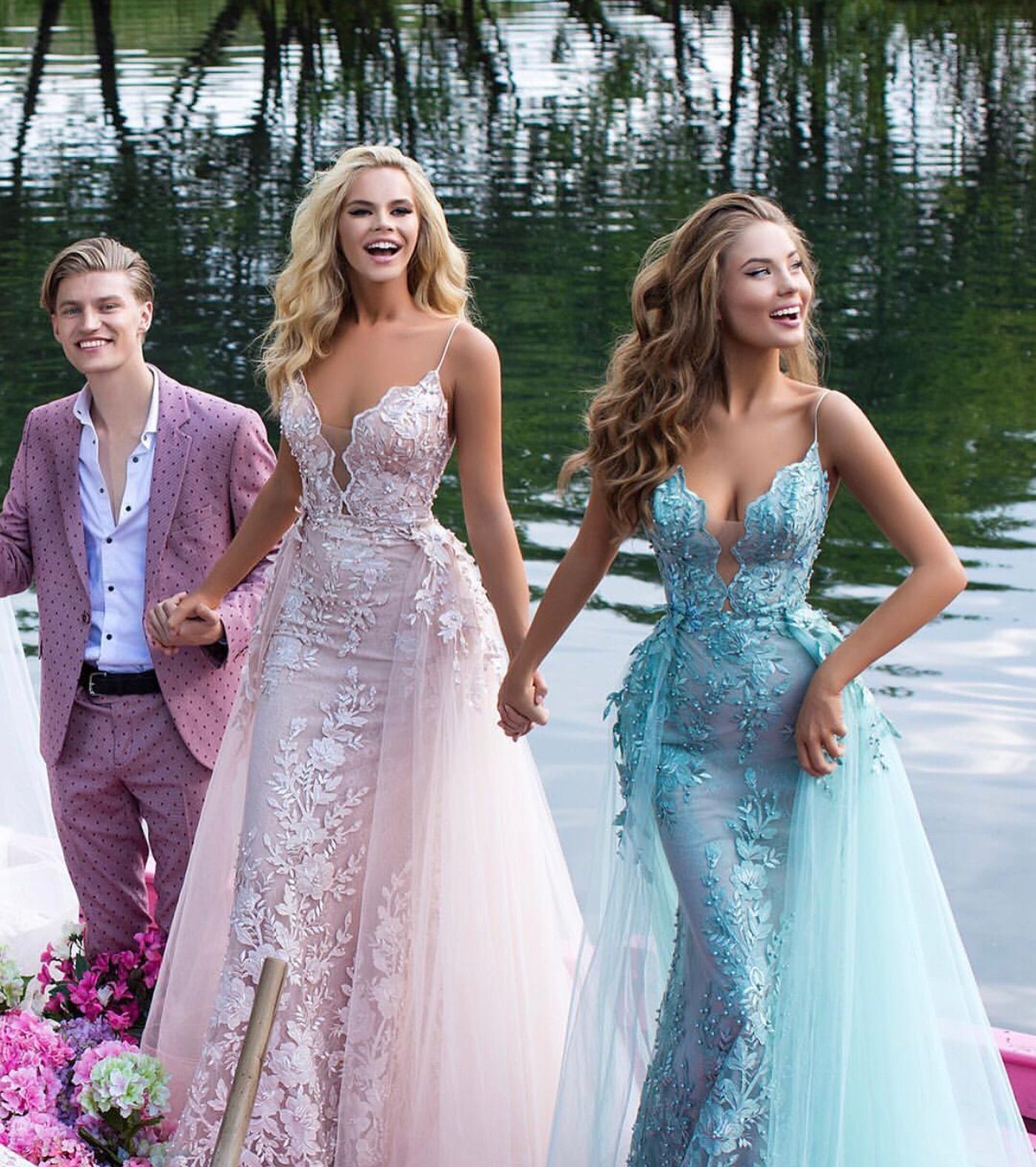 Three models in pastel formal gowns posing by a lakeside