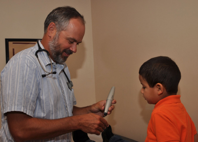 A doctor is talking to a young boy who is wearing an orange shirt.