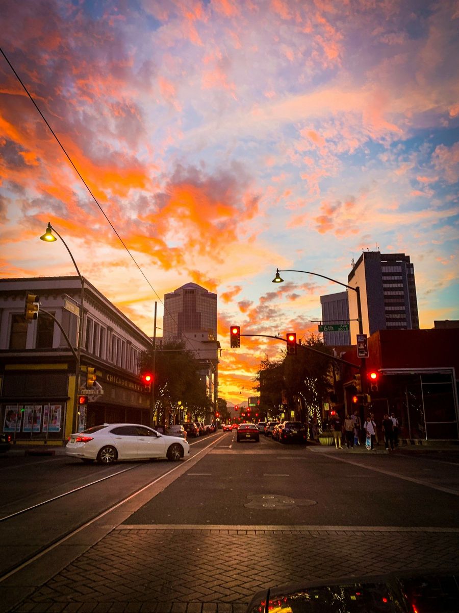 Sunset over a city street with glowing orange clouds, traffic lights, and cars at an intersection