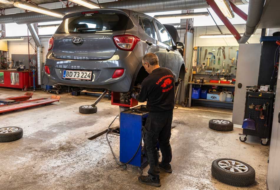 Mekaniker arbejder på en grå bil, der er blevet løftet i et autoværksted.