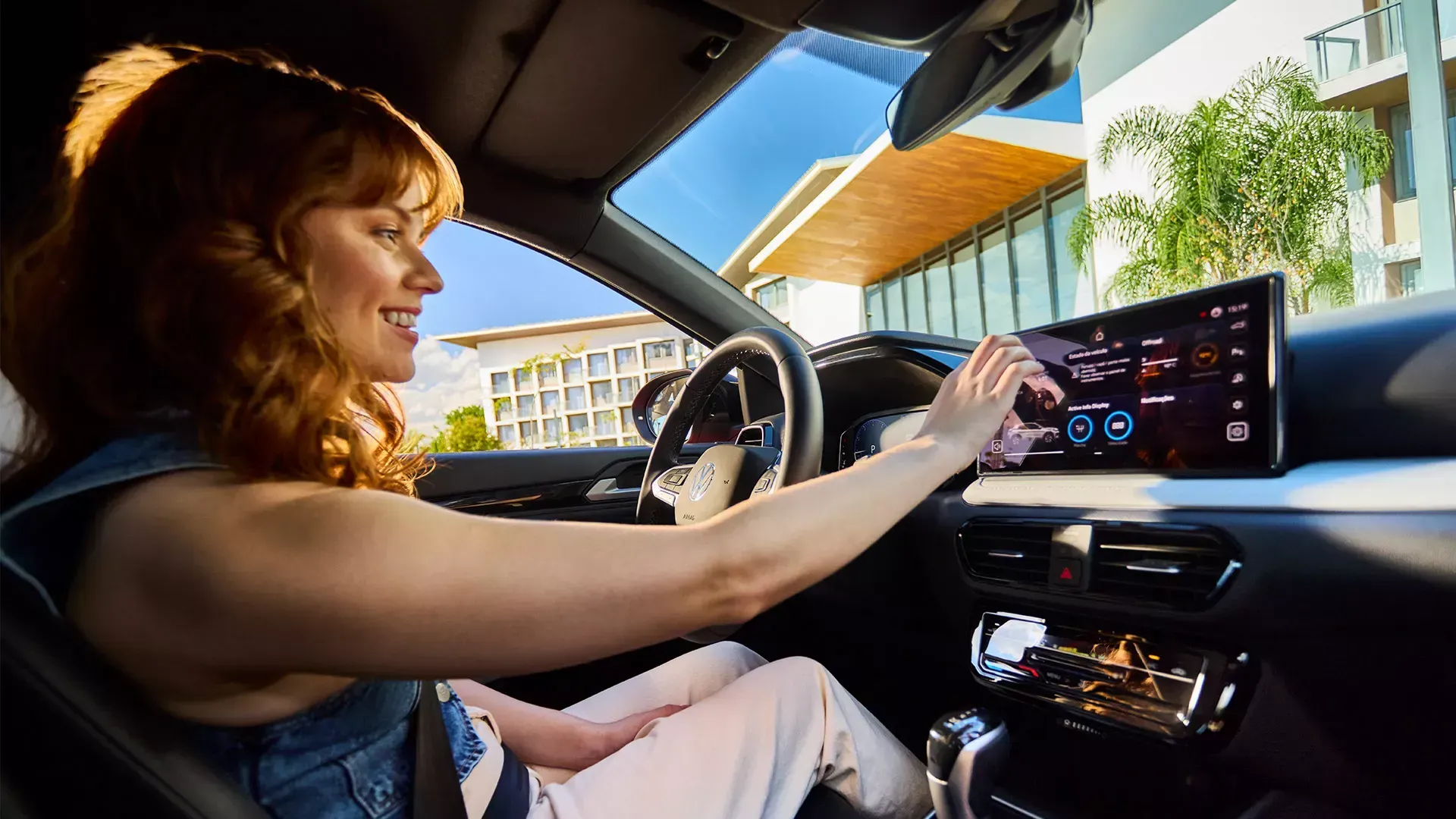 Mulher no carro usando tela sensível ao toque; fundo externo ensolarado.