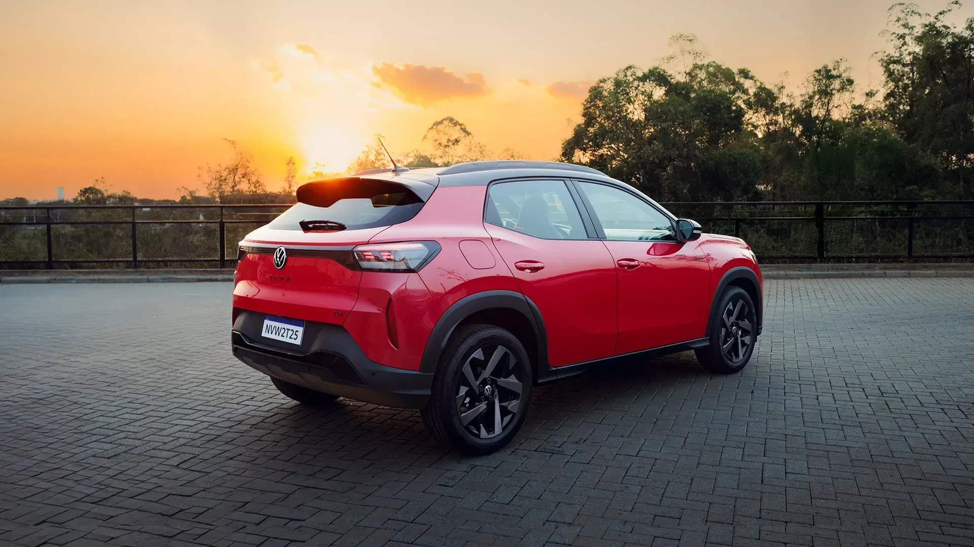 SUV compacto vermelho estacionado em paralelepípedos com o pôr do sol ao fundo.