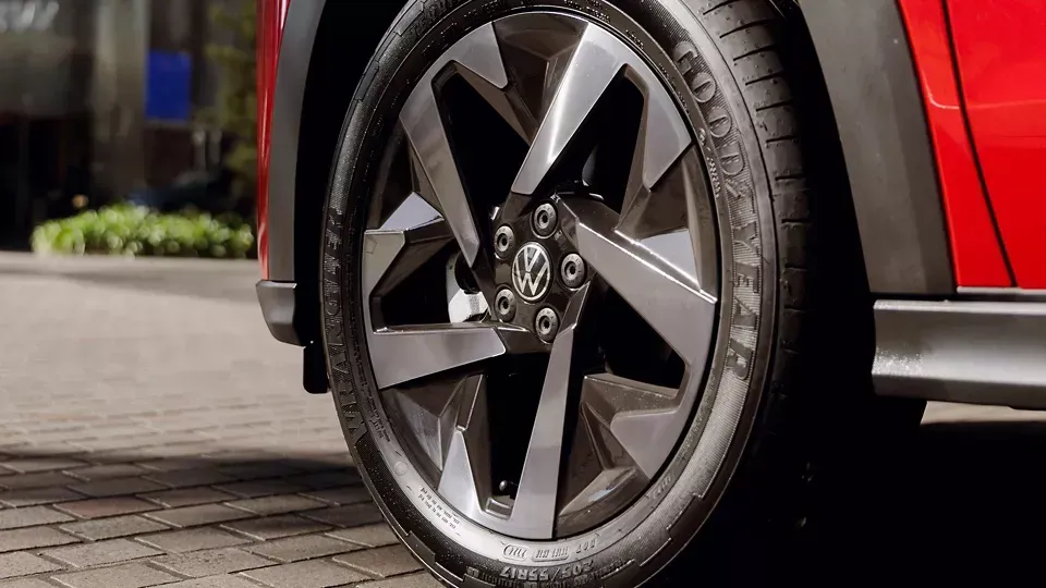 Close de uma roda de carro com um design característico em cinza escuro e prata; uma carroceria vermelha visível.