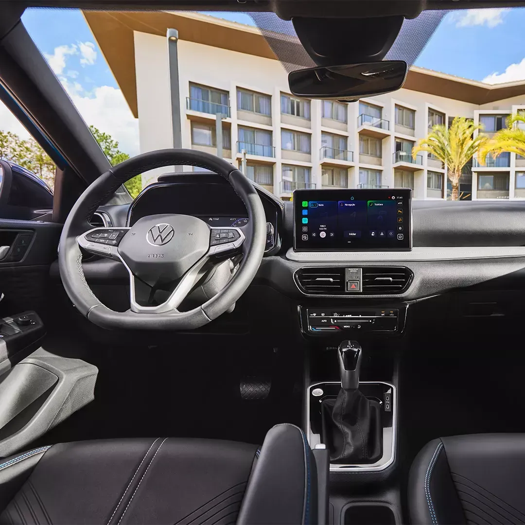 Visão interna do painel de um carro moderno: volante, tela de infoentretenimento, alavanca de câmbio e bancos de couro preto.