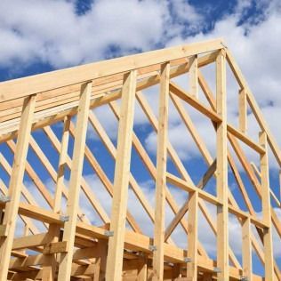 Wooden house frame under construction against a blue sky with clouds