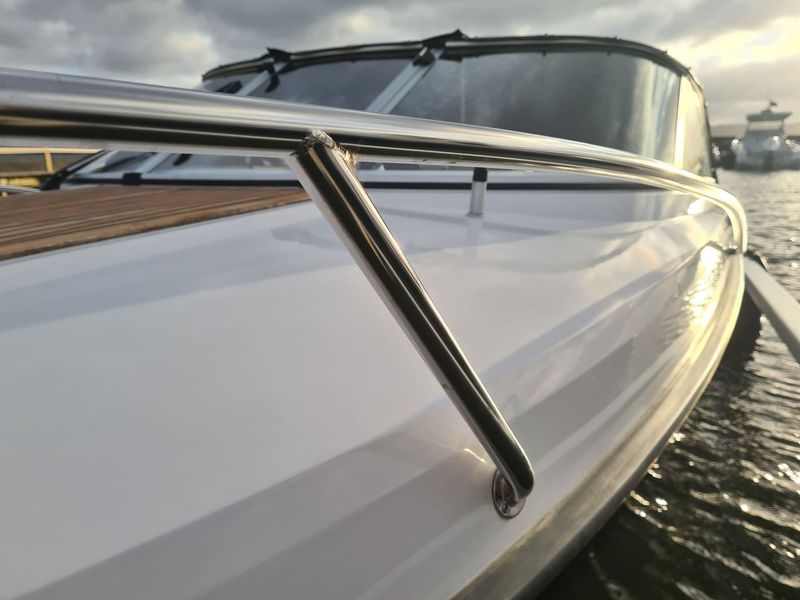 A white boat with a stainless steel railing is docked in the water