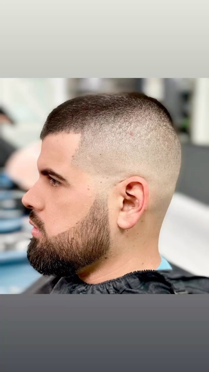Side-profile haircut with a faded buzz cut and dark beard against a blurred background