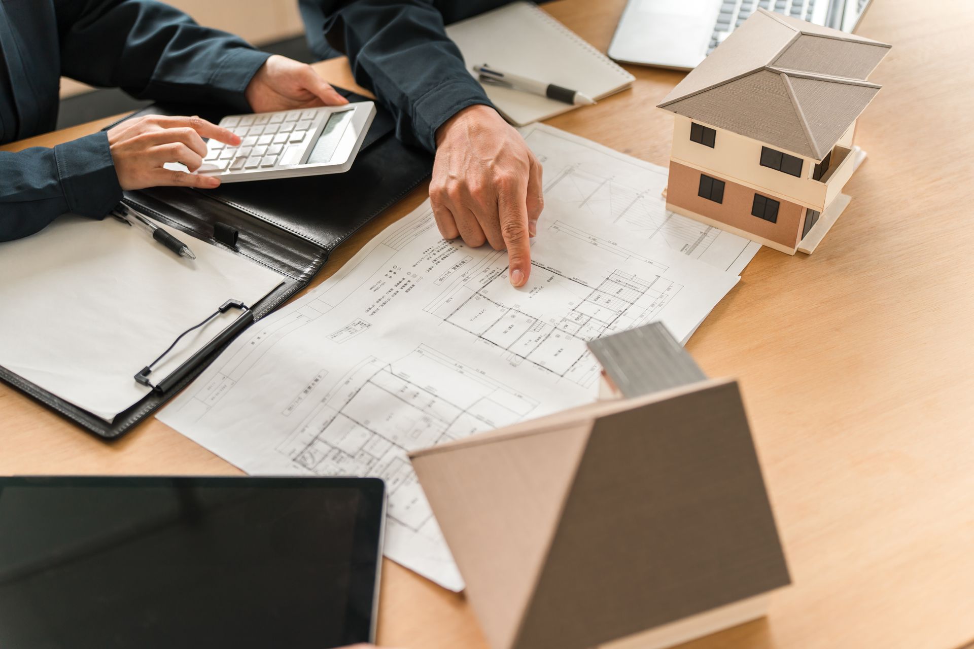 Hands reviewing house blueprints with calculator and model home on a desk