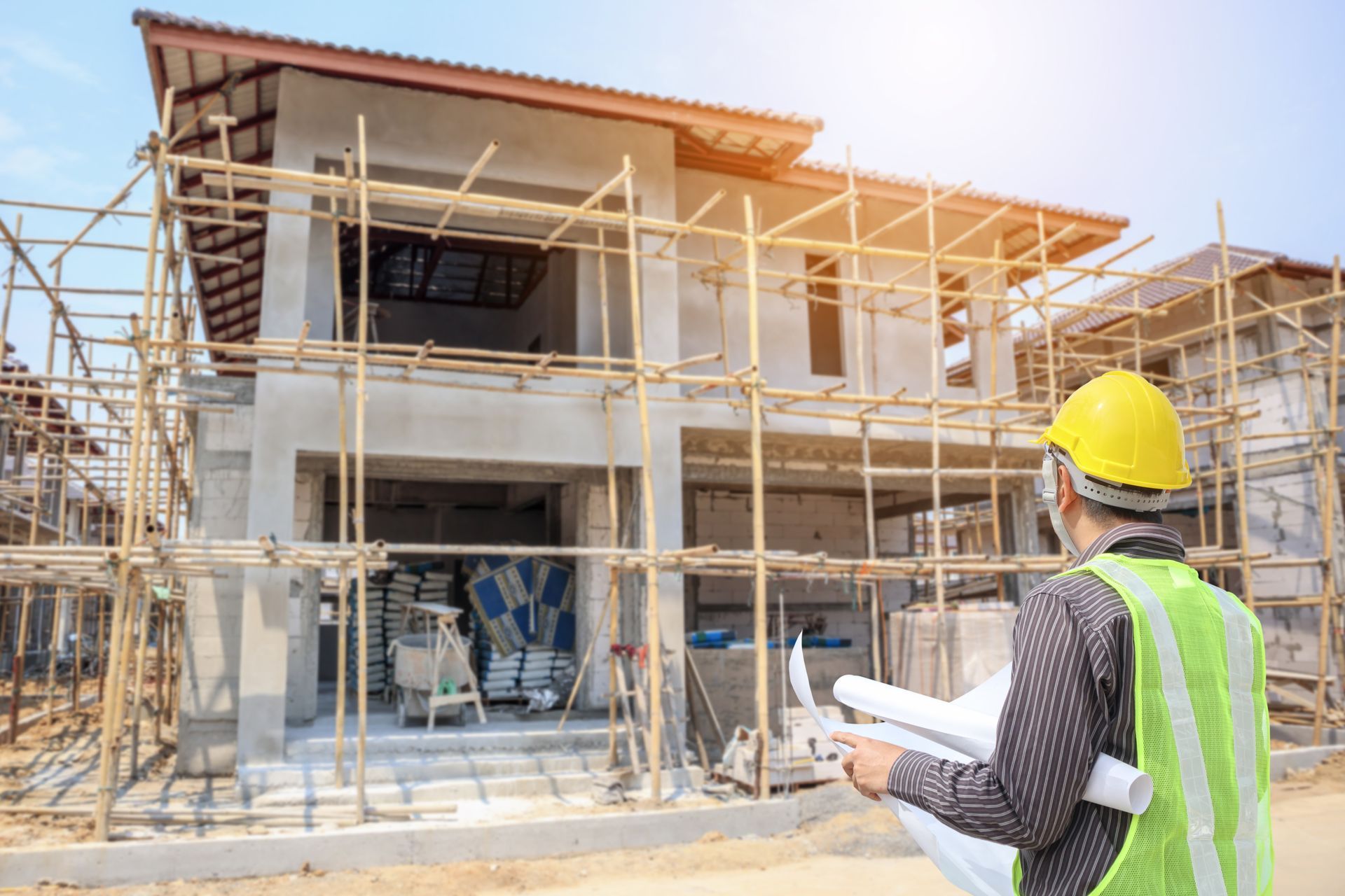 Engineer in a hard hat reviews blueprints outside a home under construction.