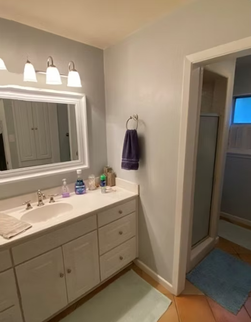 Bathroom with a white vanity, a mirror, and a shower with a blue rug and tile flooring.