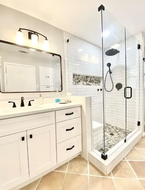 Modern bathroom with white cabinets, glass shower, and black fixtures.