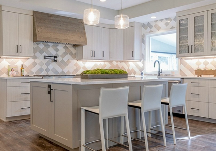 Modern kitchen with light gray cabinetry, island with white bar stools, and geometric backsplash.