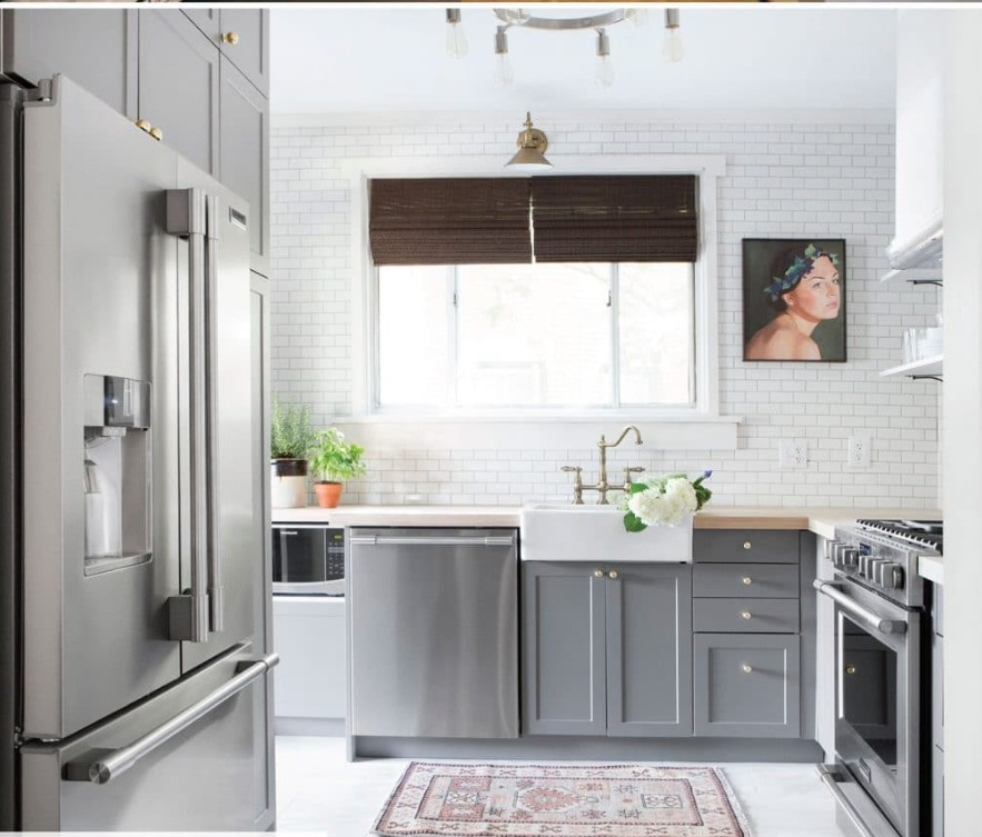 Gray and white kitchen with stainless steel appliances, white subway tile backsplash, and a brown window shade.