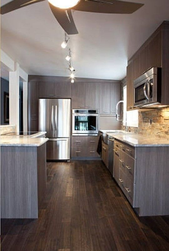 Modern kitchen with gray cabinets, stainless steel appliances, and dark wood floors.