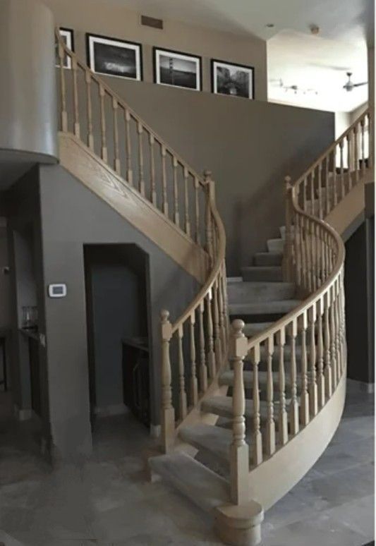 Wooden staircase with two curving flights, gray walls, and three framed photos.