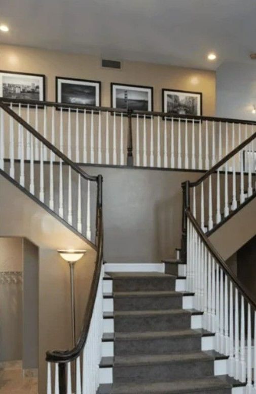 A two-story entryway with a staircase, framed black-and-white photos, and a floor lamp.