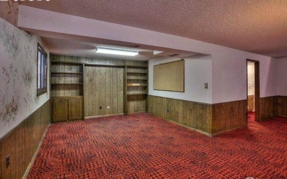 Empty basement with red carpet, wood paneling, built-in shelves, and a large bulletin board.
