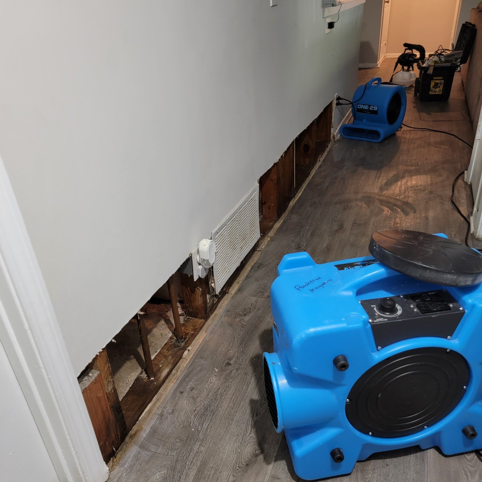 Blue air movers drying a hallway wall with exposed studs and damaged drywall