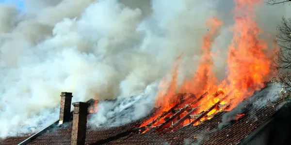 Rooftop fire with thick gray smoke and bright orange flames spreading across the roof