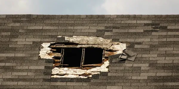 Damaged roof with a broken skylight and exposed shingles around it