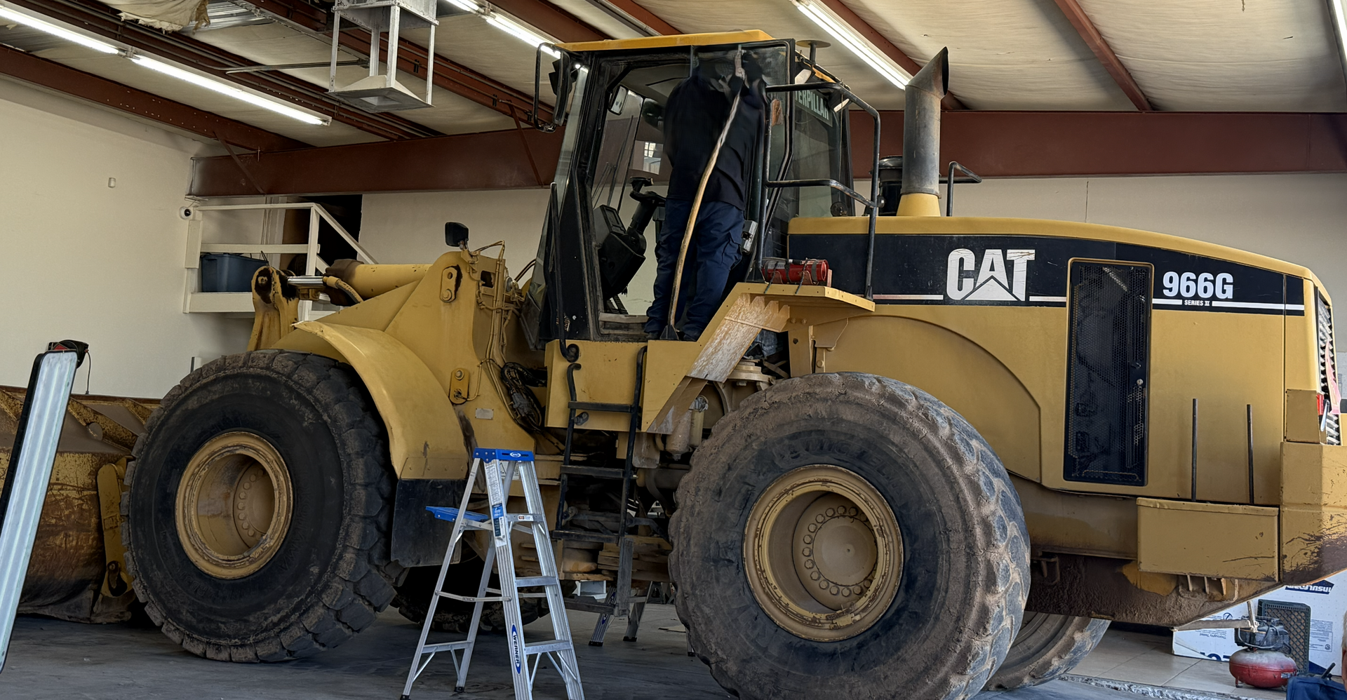 Yellow Caterpillar 988G front-end loader inside a garage. A person is inside the cab.