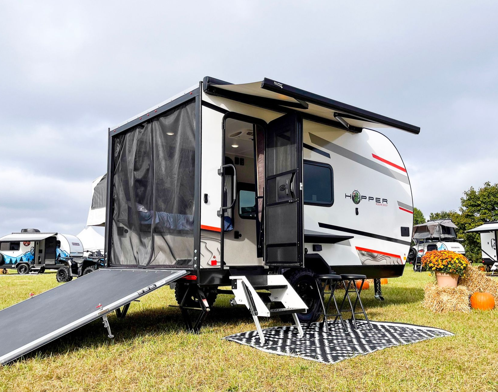 White RV trailer with awning and ramp on a grassy campsite