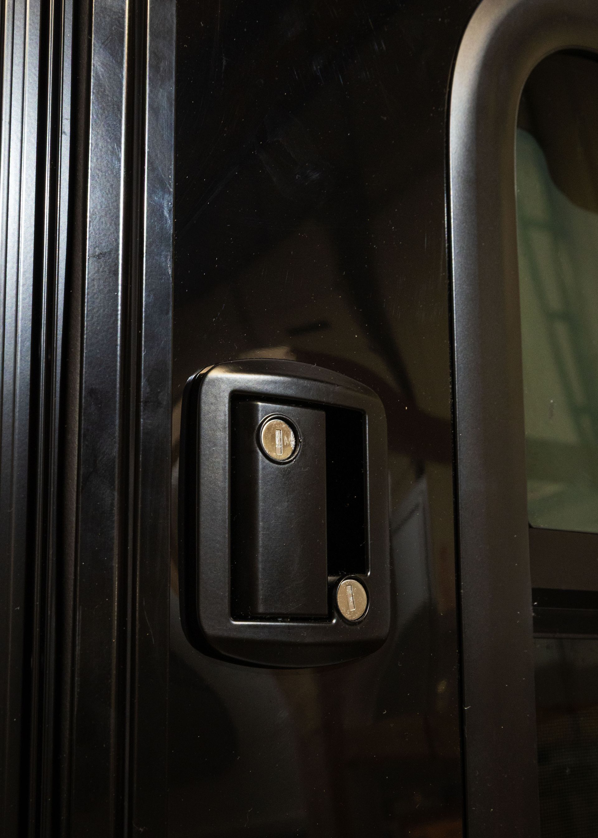 Close-up of a black door handle on a dark vehicle door with two brass screws