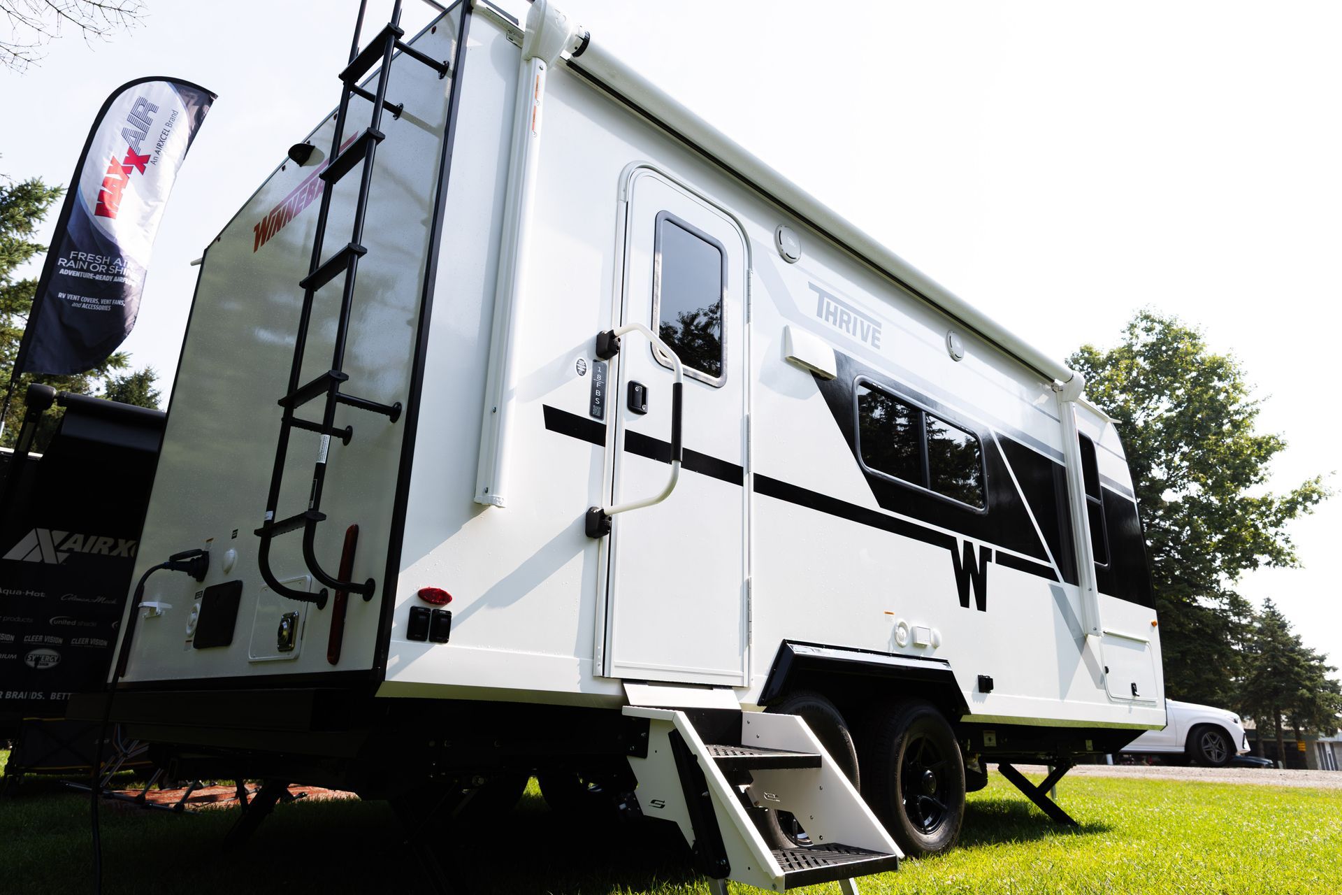 White travel trailer camper parked on grass, side view with black accents and awning, outdoors