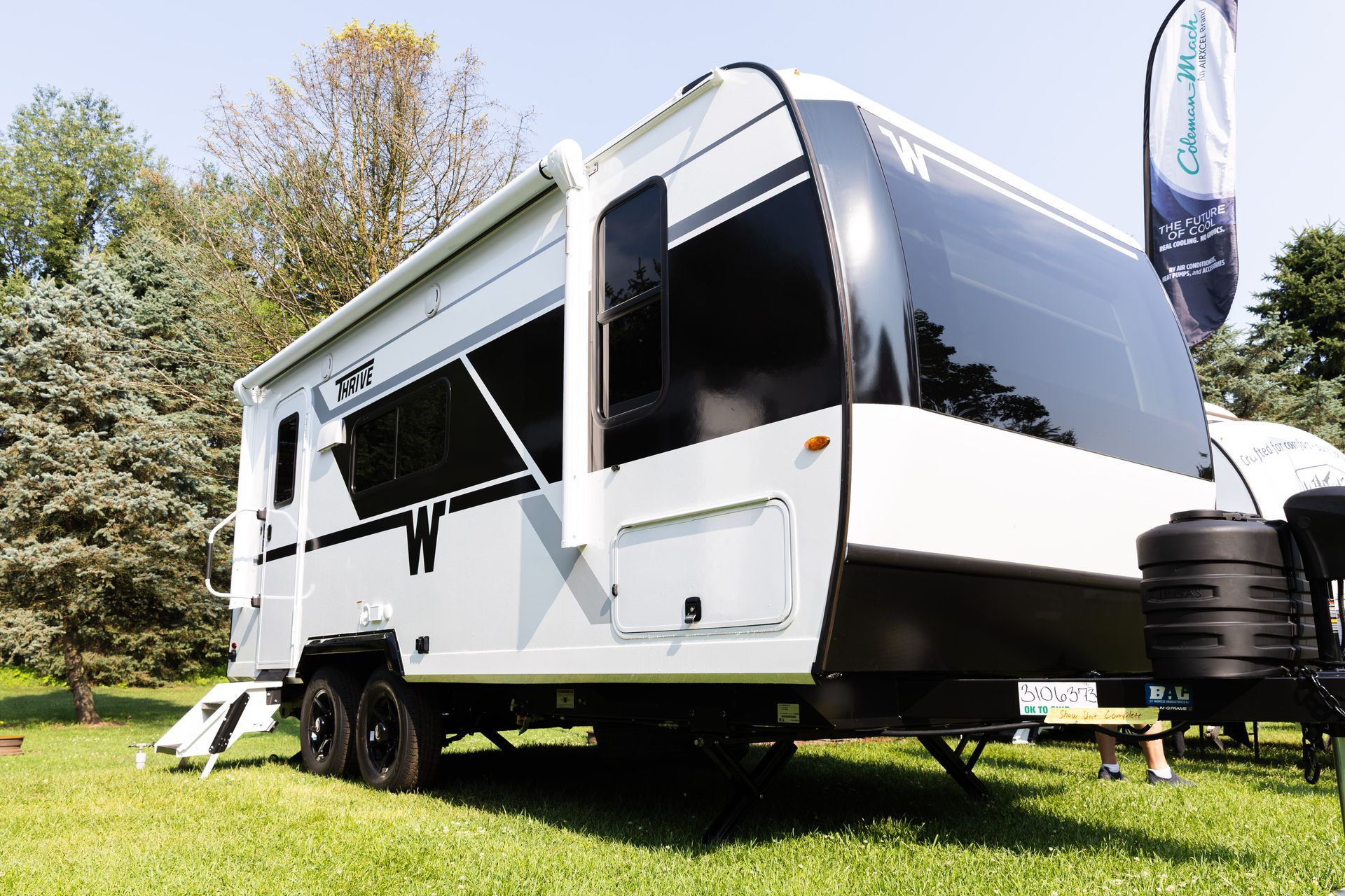 White travel trailer parked on grass under trees, with an awning extended.