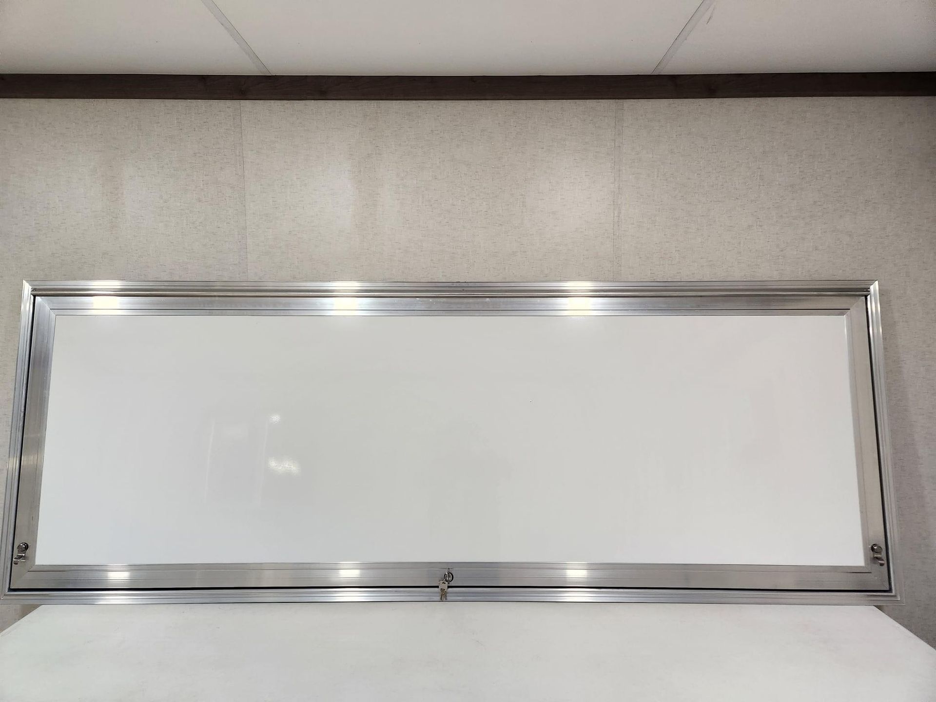 Empty whiteboard with silver metal frame mounted on a light gray wall.