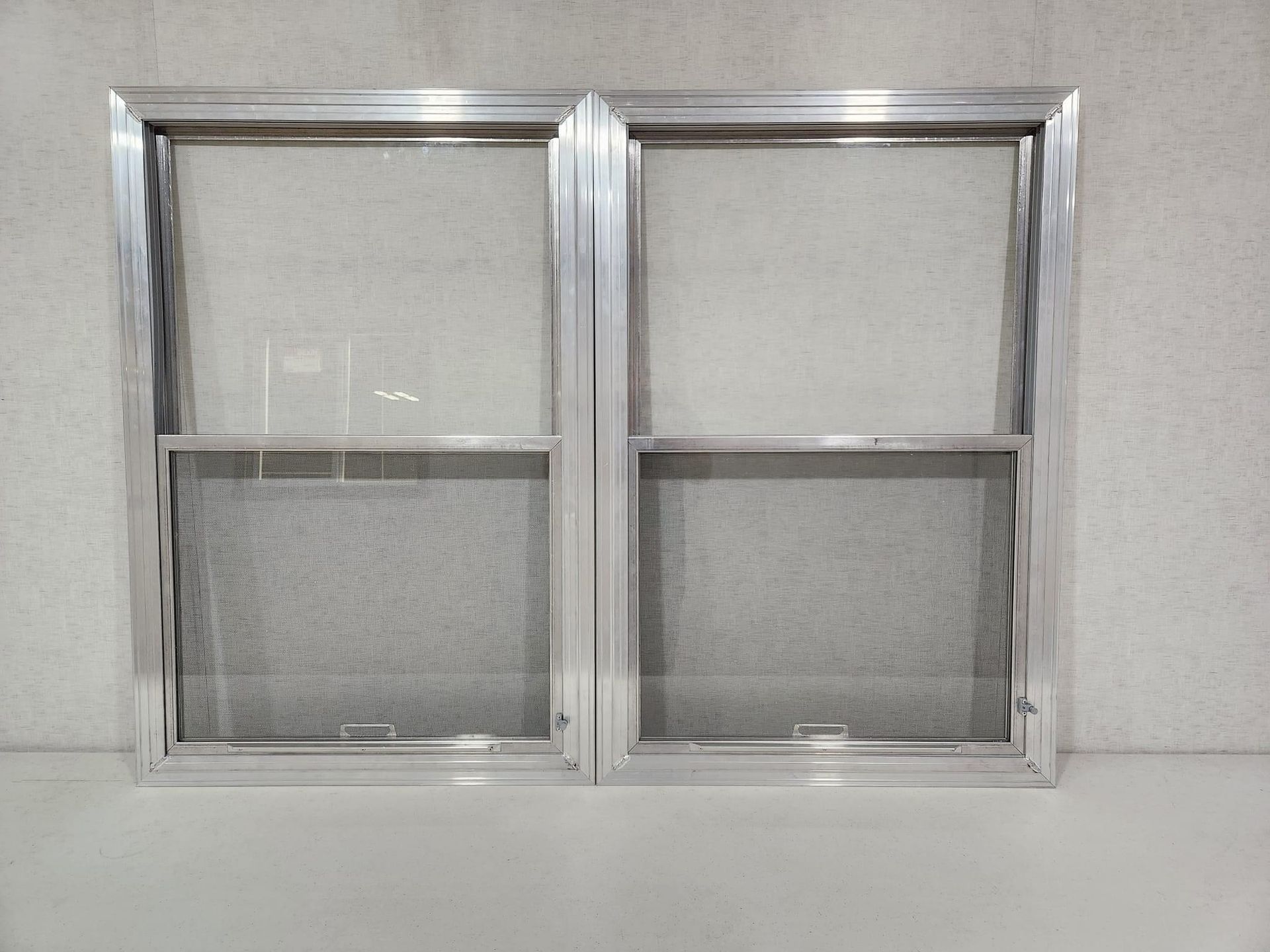Two aluminum window screens leaning against a white wall
