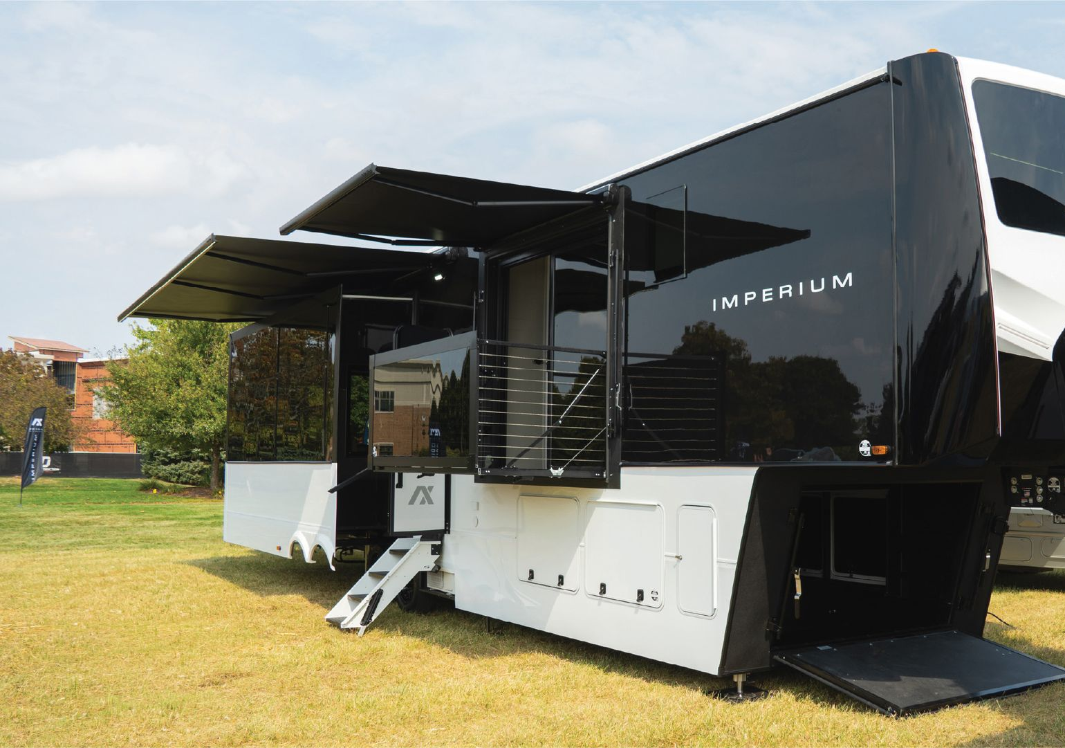 Black Impalium camper trailer with awning and steps parked on grass under a blue sky