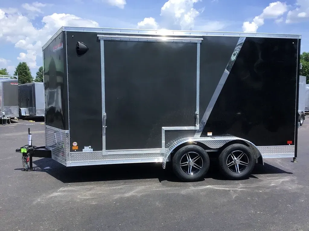 Black enclosed cargo trailer with tandem wheels parked on pavement under a cloudy sky