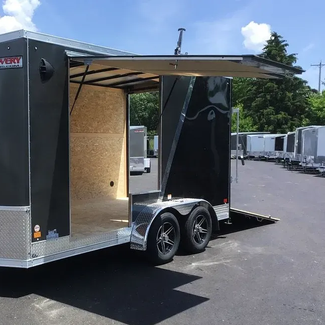Open black cargo trailer with ramp door parked on asphalt lot, another trailer in the background