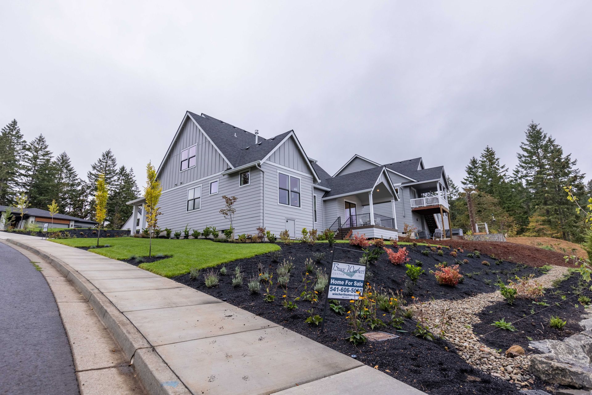 Modern gray house with landscaped hillside and sidewalk on an overcast day