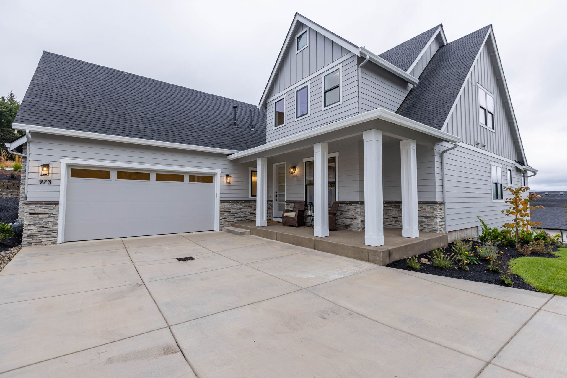 Modern gray two-story suburban house with a white garage, front porch, and wide concrete driveway
