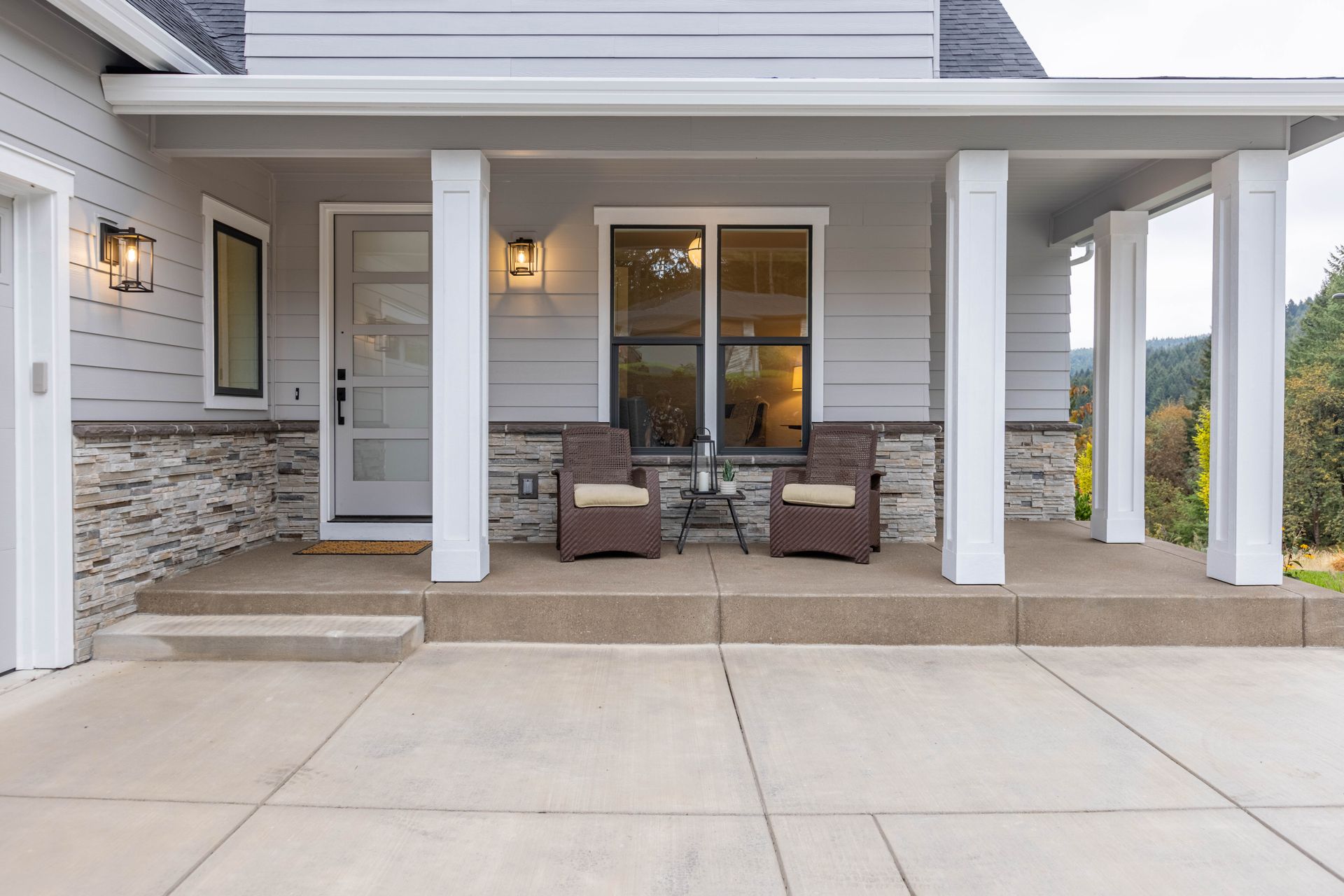 Covered front porch with stone accents, white columns, sliding glass doors, and patio chairs on a concrete patio.