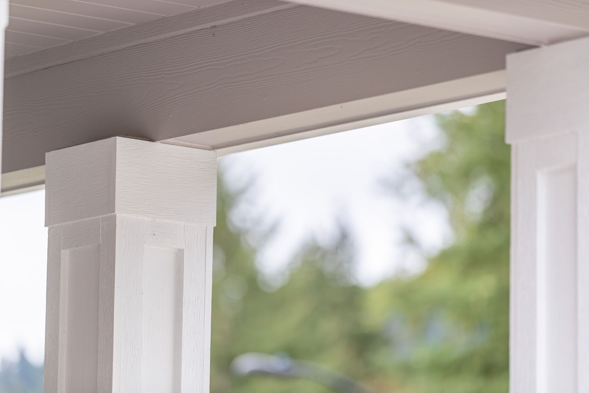 White porch columns under a ceiling, with blurred green trees in the background.