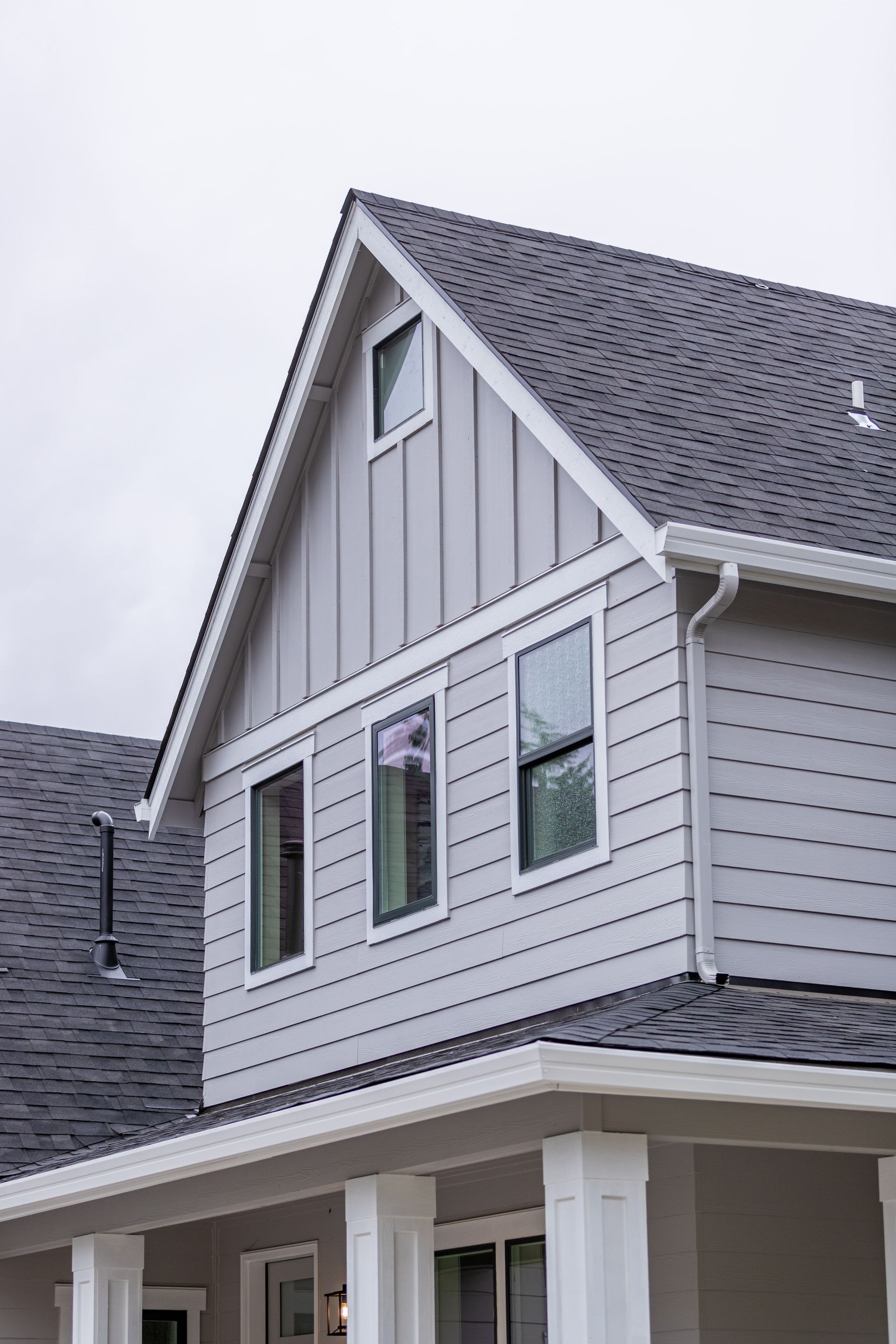 Gray two-story house with gabled roof and white trim against a cloudy sky