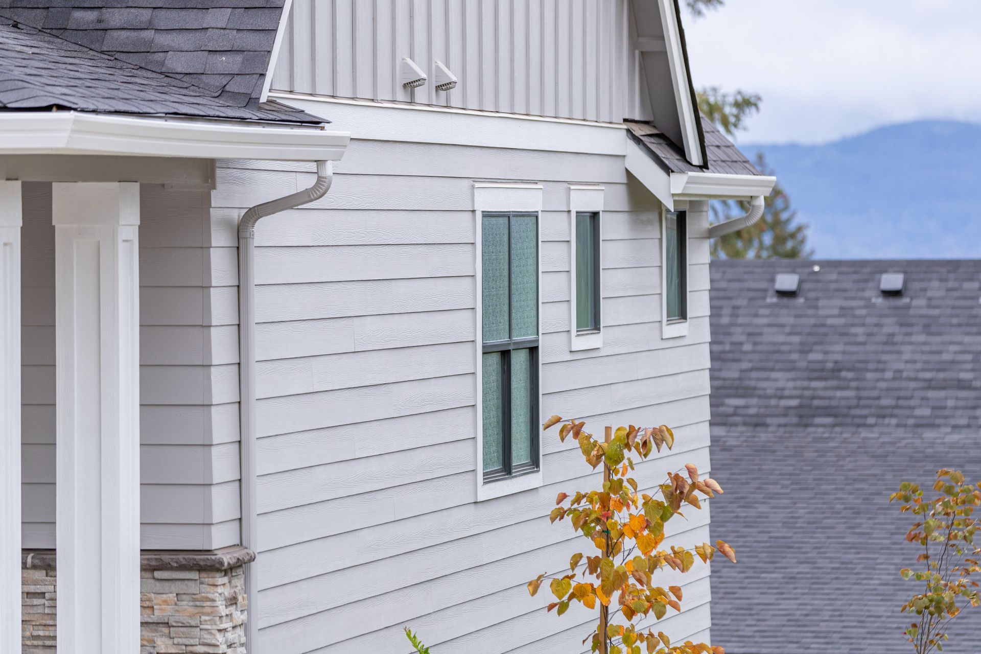 White house siding with green shutters and gray roofs, viewed from a hillside with autumn foliage.