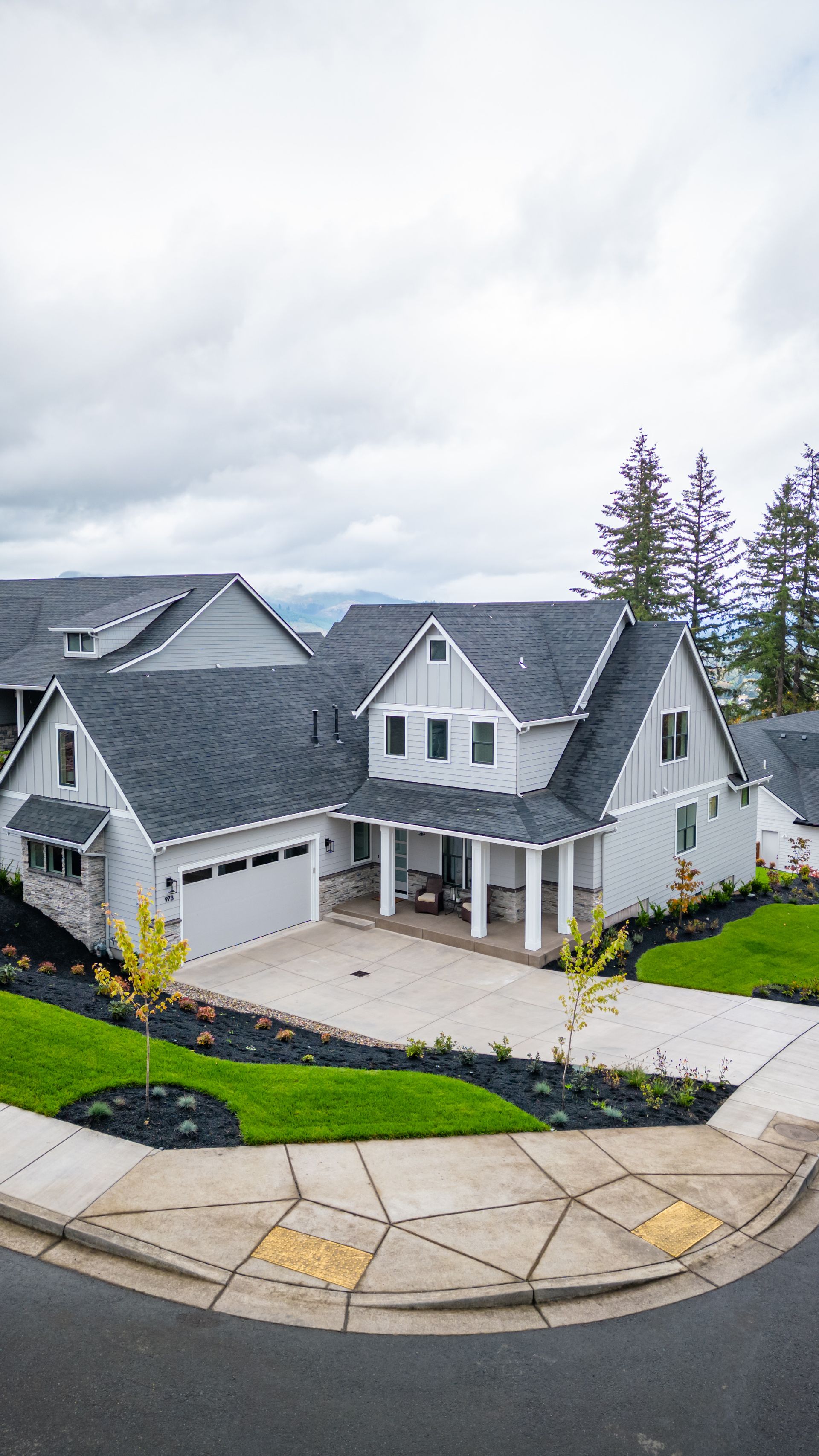 White two-story suburban house with gray roof, front porch, garage, and curved driveway on a cloudy day